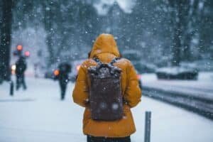 thom-holmes-9gbwzrbt0qu-unsplash6447765943648161456jpg | Pugnalom Person seen from behind wearing a bright orange winter coat and a dark backpack, walking through falling snow in a city street.