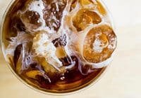 Top-down view of a glass filled with iced coffee, ice cubes and milk swirls visible from above.”] ,