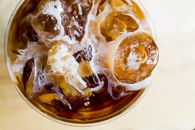 Top-down view of a glass filled with iced coffee, ice cubes and milk swirls visible from above.”] ,