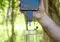 Hand holds a smartphone connected to a small sensor dipping into a glass of water outdoors.