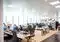 Open-plan office with employees working at desks and computers under bright ceiling lights.